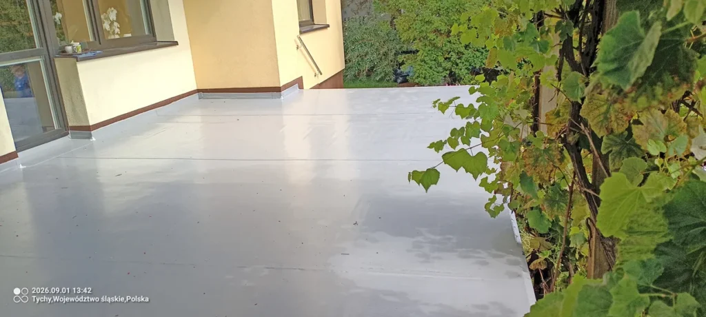 Jasna membrana PVC na tarasie przy domu w Tychach, wykończona przy balustradzie i roślinach.